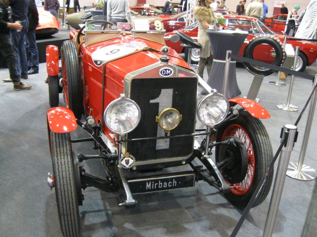 Ein roter Oldtimer-Rennwagen mit der Nummer 1 auf dem Kühlergrill, ausgestellt auf der Techno Classica Essen 2015, mit anderen Oldtimern und Besuchern im Hintergrund.