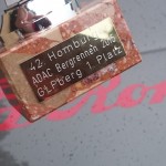 Nahaufnahme einer Trophäe mit der Aufschrift „42. Homburger ADAC Bergrennen 2005 G.L.P. Berg 1. Platz“, platziert auf einer Fläche mit dem Alfa Romeo-Logo.