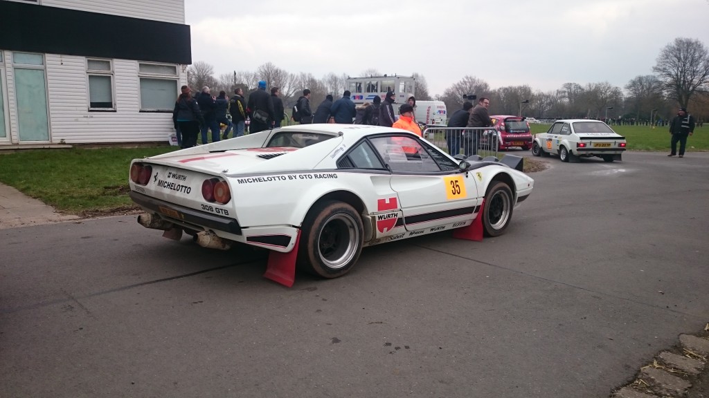 Ein weißes Rennauto mit der Aufklebernummer 35 steht auf einer gepflasterten Fläche bei Race Retro 2016. Menschen haben sich um das Auto versammelt, im Hintergrund sind Gebäude und andere Autos zu sehen.