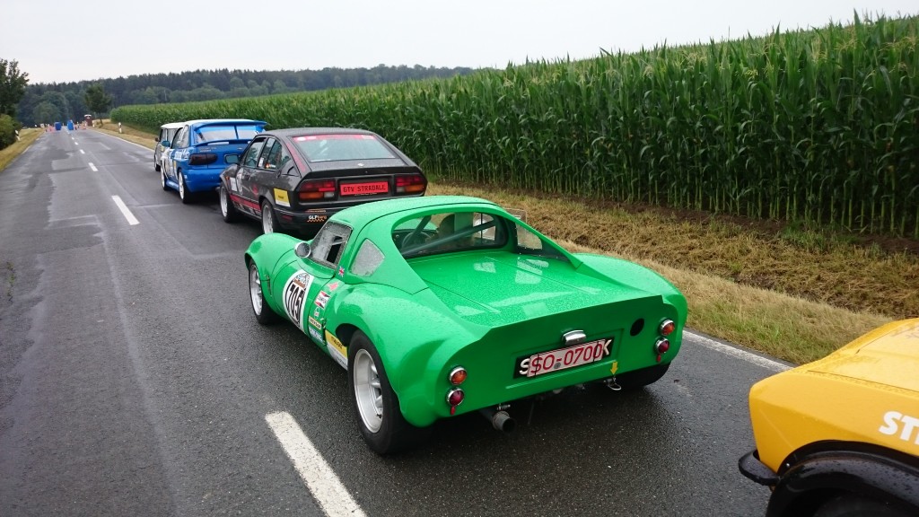 Eine Reihe historischer Rennwagen, darunter ein grüner Sportwagen mit dem Kennzeichen „SGO 0700K“, parkt während des Weserbergpreises 2016 auf einer Landstraße neben einem Maisfeld. Im Hintergrund sind Bäume zu sehen.