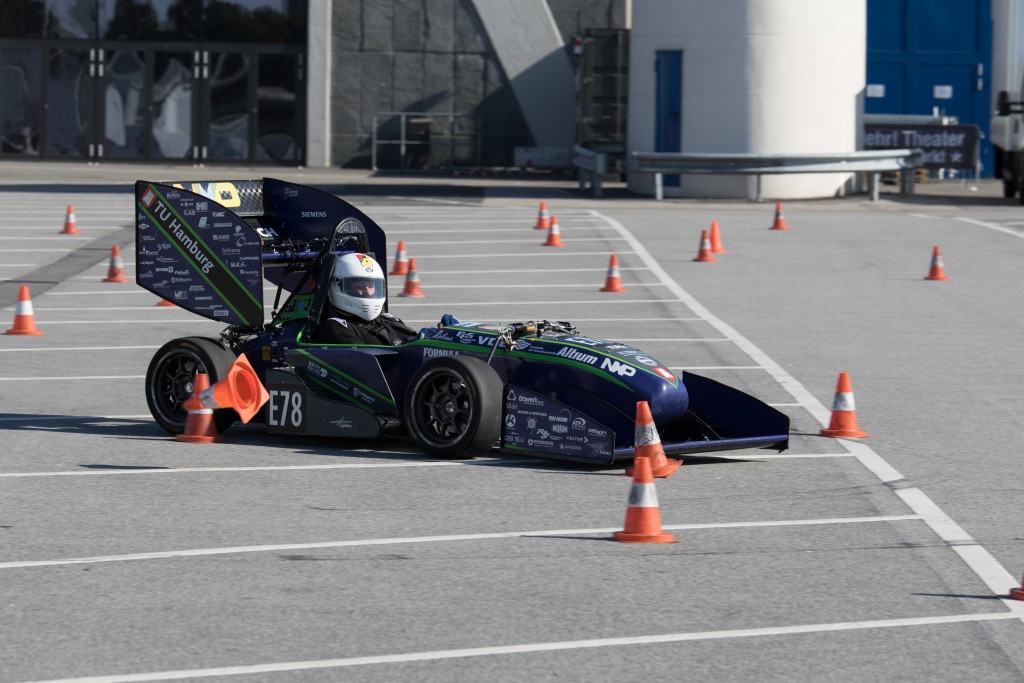 Eine Person mit Helm fährt einen Formula-Student-Rennwagen mit der Aufschrift „E78“ durch eine mit orangefarbenen Pylonen markierte Strecke.