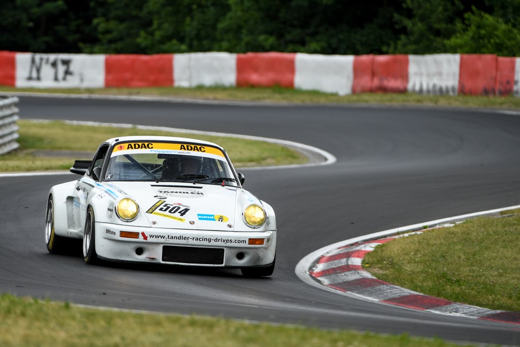 Ein weißes Rennauto mit gelben Akzenten und der Nummer 804 auf der Motorhaube fährt auf einer kurvenreichen Rennstrecke, die von roten und weißen Barrieren gesäumt und von Grün umgeben ist.