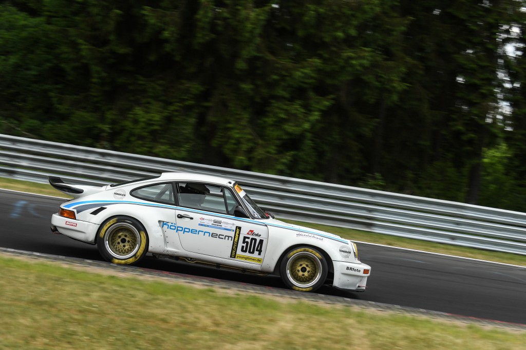 Ein weißes Rennauto mit der Nummer 504 auf der Tür fährt auf einer von Bäumen und Metallgeländern umgebenen Strecke.