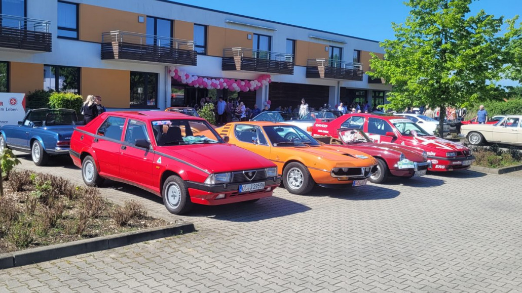 Eine Reihe klassischer Autos, darunter rote und orange Modelle, parken vor einem modernen Gebäude.