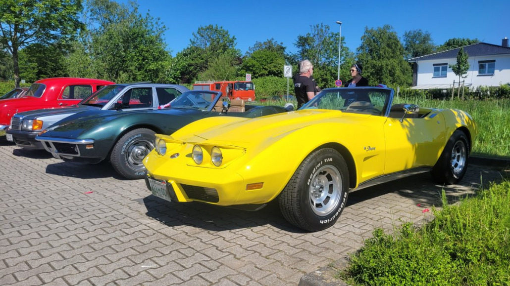 Eine Reihe im Freien geparkter Oldtimer, darunter eine gelbe Corvette-Cabriolet im Vordergrund und andere Oldtimer in der Nähe.