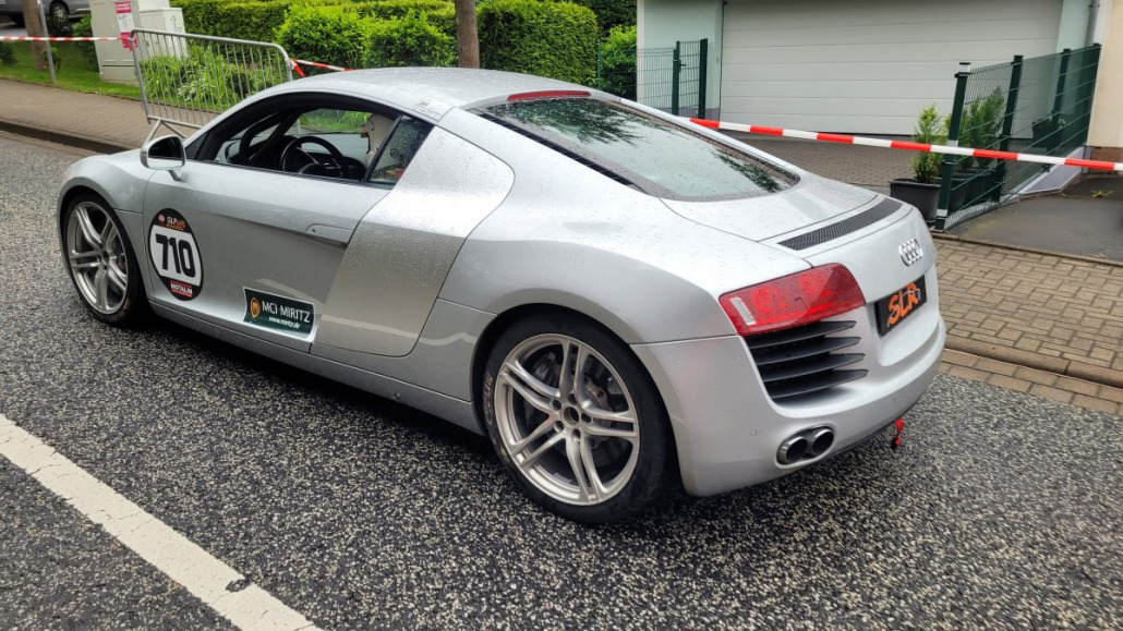 Ein silberner Audi-Sportwagen mit der Startnummer 710 parkt auf der Straße. Auf der Oberfläche des Autos sind Regentropfen zu sehen.