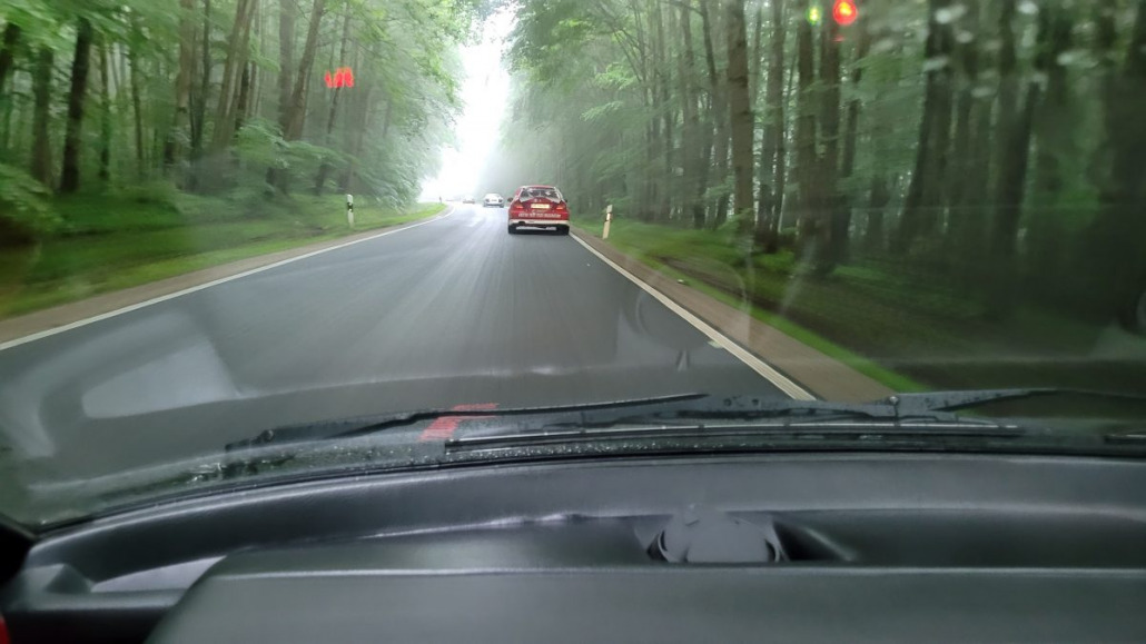 Ein Blick aus dem Inneren eines Autos, das auf einer nebligen, von Bäumen gesäumten Straße fährt, mit einem anderen Fahrzeug vor ihm. Die Straße ist leicht kurvig und auf beiden Seiten stehen dichte Bäume.